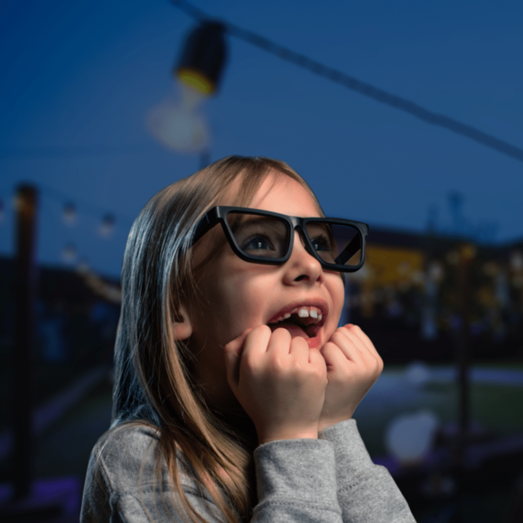 A little girl watches a movie outside on a rented J-Crew Entertainment screen with an awed expression on her face.